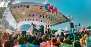 Color Manila 2025 Bühne: DJ mit Mikrofon, farbige Pulverwolken und jubelnde Menge unter Sonnendach – explosives Farbenfest und Gemeinschaftsgefühl im Freien.