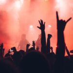 Silhouettierte Menge mit erhobenen Händen im roten Nebel vor DJ bei einem