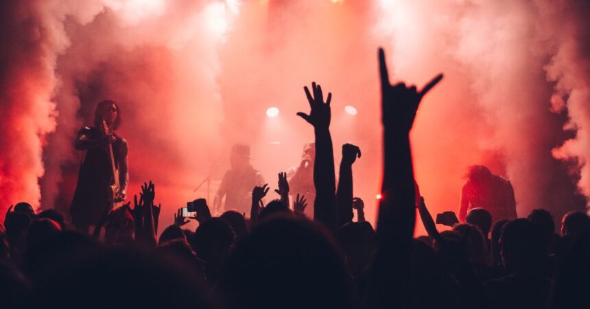 Silhouettierte Menge mit erhobenen Händen im roten Nebel vor DJ bei einem