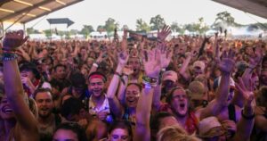 Jubelnde Menge mit hochgereckten Händen und Glitzer im Sonnenuntergang bei einem Electro-Festival 2025