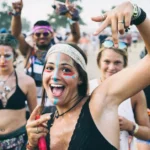 Fröhliche Raverinnen bei Techno-Festival 2025: buntes Facepaint, Festival-Bändchen und Peace-Zeichen – Sommer-Vibes, Gemeinschaftsgefühl und pure Lebensfreude im Freien.