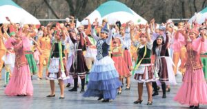 Jugendliche Festivaltänzer in bunten Trachten führen einen traditionellen Volkstanz auf, fröhliche Choreographie, lebhafte Festplatz-Atmosphäre und kulturelles Erbe.