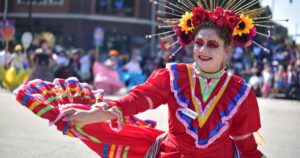 Fröhliche Tänzerin in rotem mexikanischem Trachtenkleid mit Blumenkranz und Calavera-Schminke wirbelt bei der Karneval-der-Kulturen-Parade in Berlin vor jubelndem Publikum.